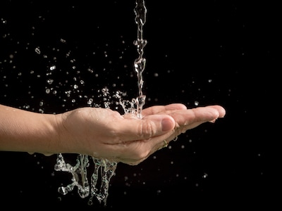 Zwei ausgestreckte Hände werden unter fließendes Wasser gehalten.
