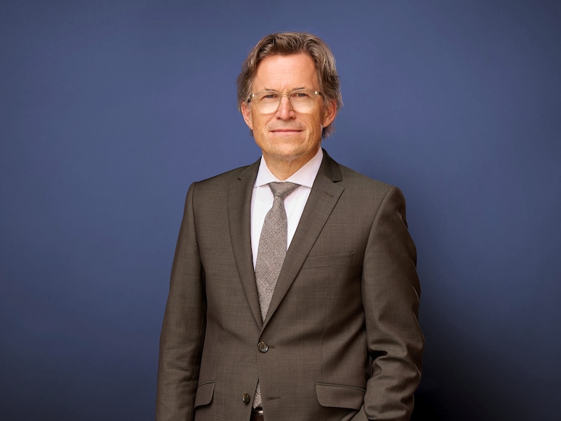 Portrait von Markus Mosa vor neutralem Hintergrund. Er trägt ein braunes Sakko.