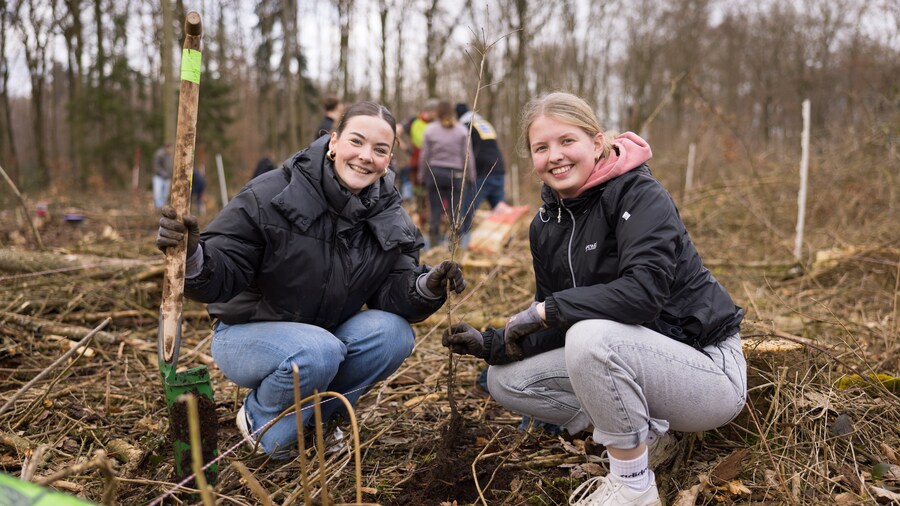 EDEKA Minden-Hannover Azubi-Baumpflanzaktion 2024 - 2 Azubis sitzen in der Hocke und lächeln freundlich in die Kamera