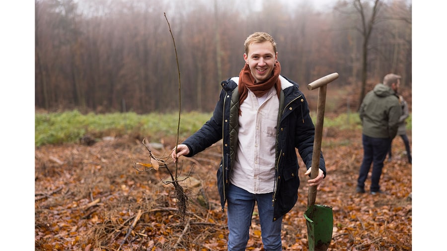 EDEKA Minden-Hannover Azubi-Baumpflanzaktion 2024 - Helfer mit Setzling und Schaufel in der Hand lächelt freundlich