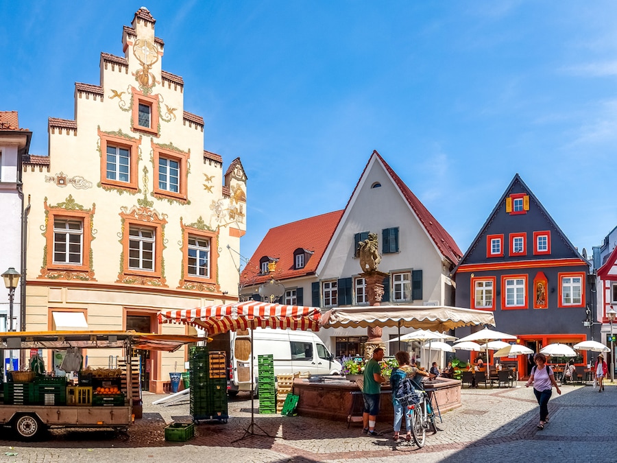 Marktstände stehen auf einem Platz in der Stadt, umgeben von schönen historischen Häusern und blauem Himmel.