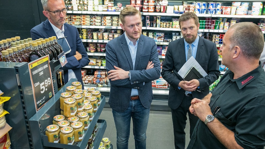 In einem Einkaufsmarkt unterhalten sich drei Männer in Sakkos mit einem EDEKA-Mitarbeiter.