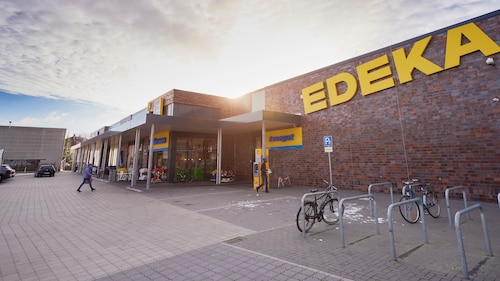 Eingang eines EDEKA-Marktes unter einem sonnigen, bewölkten Himmel.