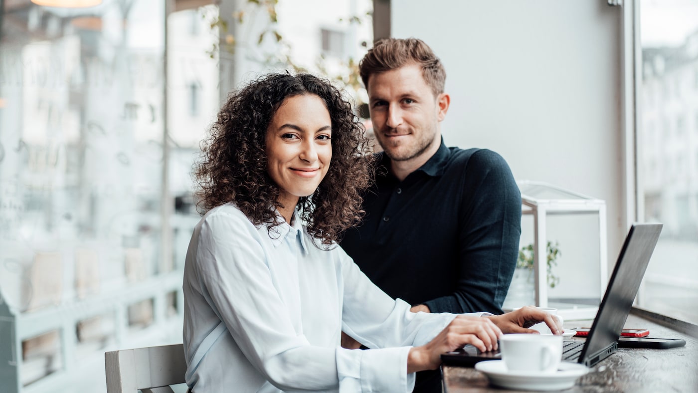 Frau und Mann sitzen am Tisch und schauen in die Kamera.