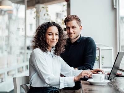 Frau und Mann sitzen am Tisch und schauen in die Kamera.