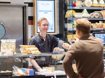 Mitarbeiter an der Bedientheke reicht Käse an