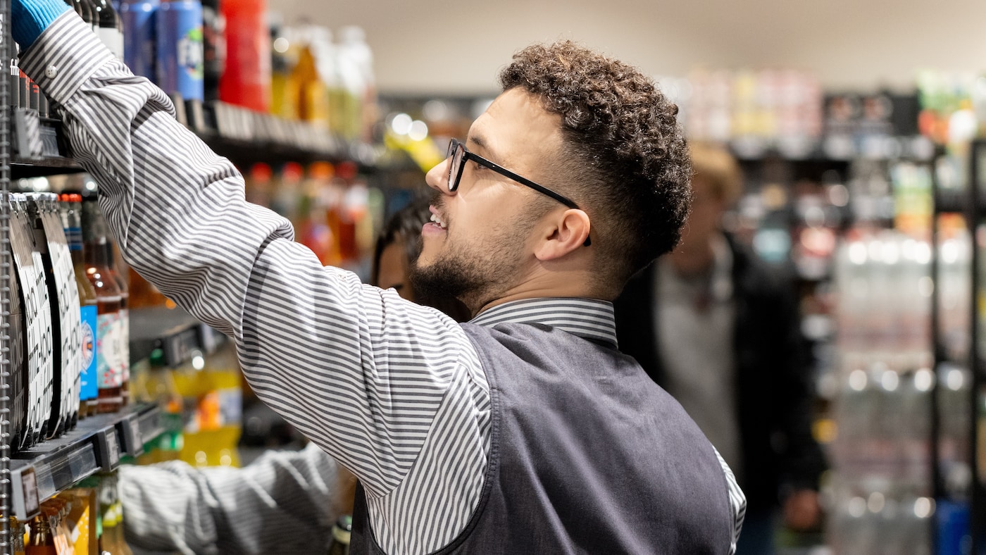 Junger Auszubildender räumt Ware in ein Getränkeregal