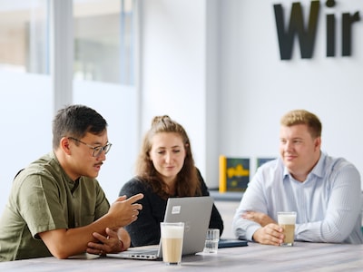 Drei Kolleg:innen im Meeting unterhalten sich angeregt.
