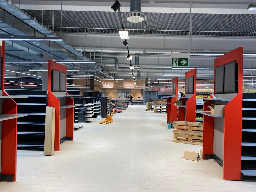 Noch leere Regale mit roten Rahmen vor dem Ende sind zu sehen, im Hintergrund die mit Holzoptik verkleideten Bedientheken.