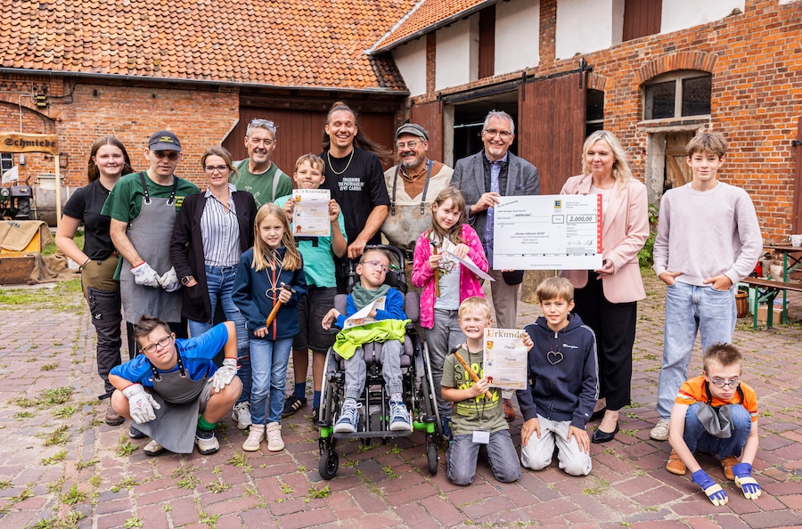Eine Gruppe von Kindern, Jugendlichen, ihre Betreuer und EDEKA-Vertreter stehen mit dem Spendenscheck vor einer Scheune.