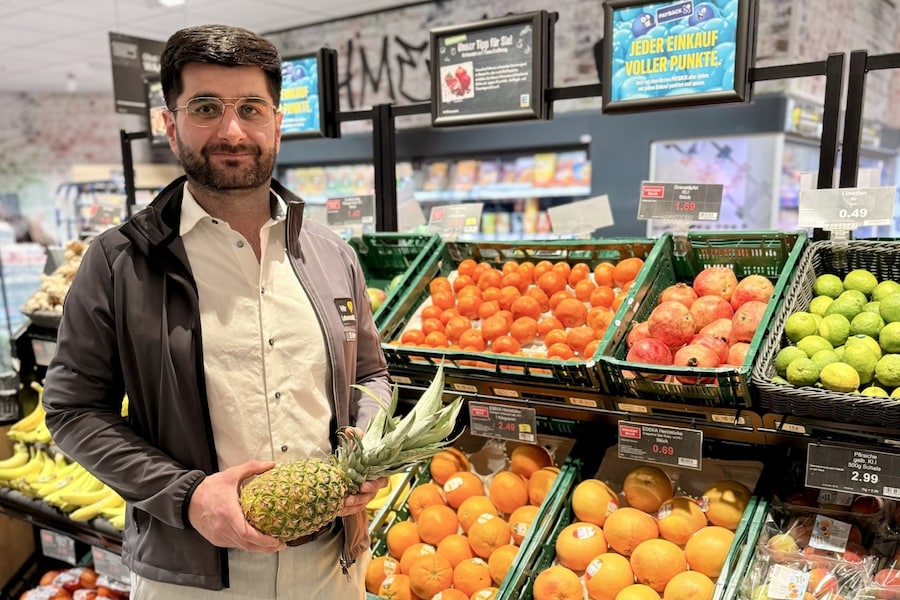 Samet Aslan steht in der Obst- und Gemüseabteilung und hält eine Ananas.