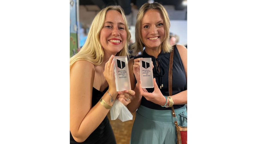 Zwei Frauen halten den Pokal vom German Brand Award in den Händen und lächeln.