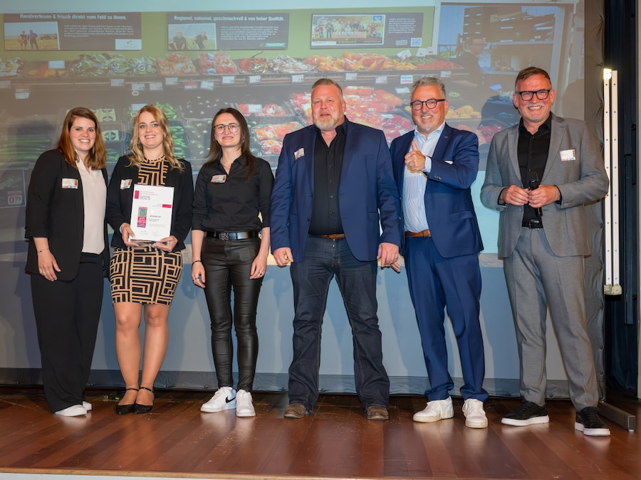 6 Personen stahlen und stehen vor einer Gemüsetheke. Eine Frau hält eine Urkunde, ein Mann hat den Daumen hoch.