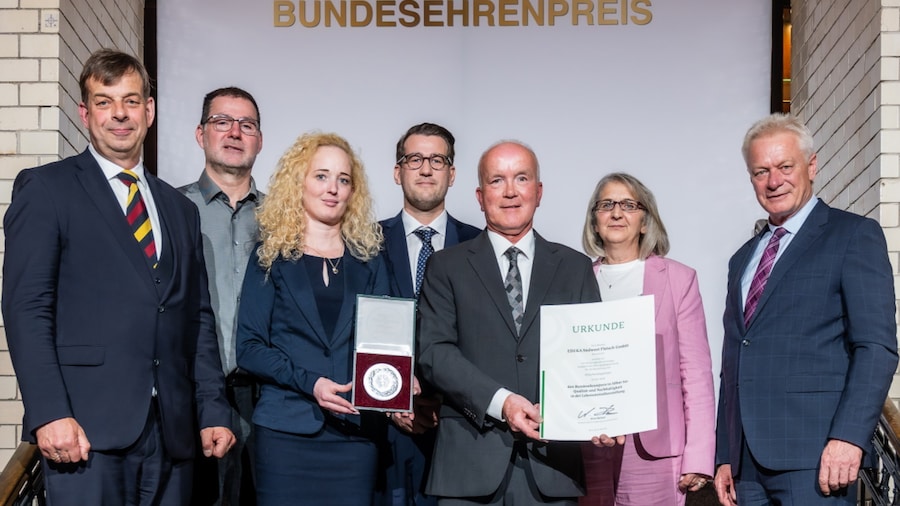 7 Personen stehen mit der Urkunde und Medaille auf einer Treppe