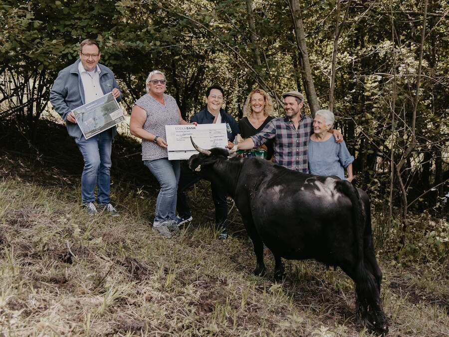 4 Frauen und 2 Männer stehen mit symbolischem Scheck vor einer Dexterkuh