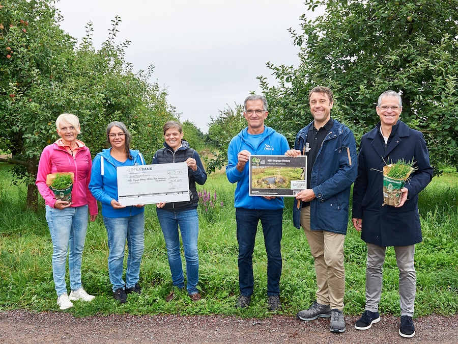 3 Frauen und 3 Männer stehen mit symbolischem Scheck und Pflanztöpfen vor einer Streuobstwiese.