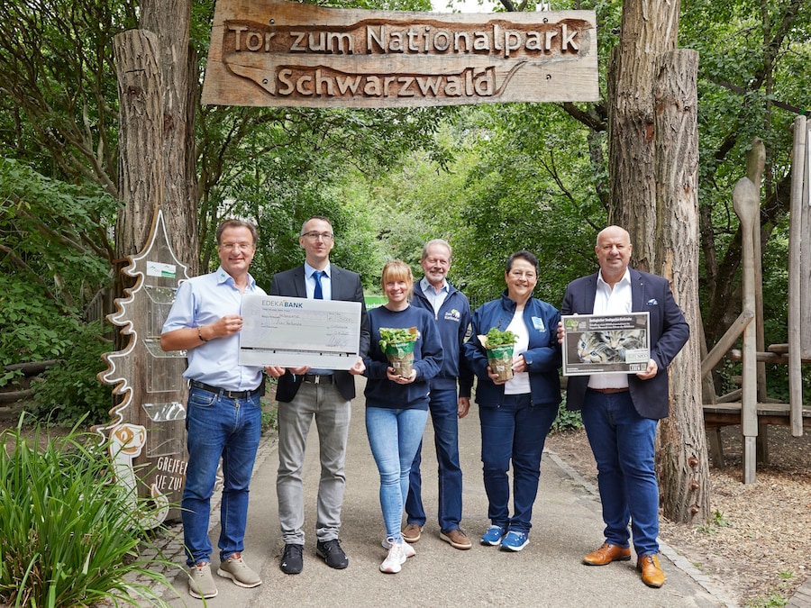 2 Frauen und 4 Männer stehen mit symbolischem Scheck und Kräutertöpfen vor dem Tor zum Nationalpark