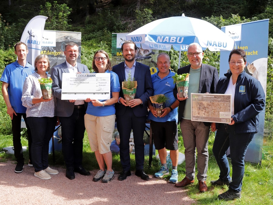 Eine Gruppe von 8 Personen steht mit symbolischem Scheck vor NABU Fahnen und Schirmen