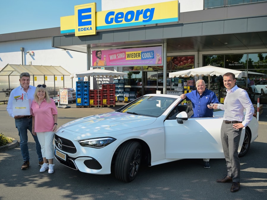 Ein Mann steht mit einem weißen Cabrio vor dem EDEKA-Markt. Daneben stehen ein Mann und eine Frau und rechts noch ein Mann.