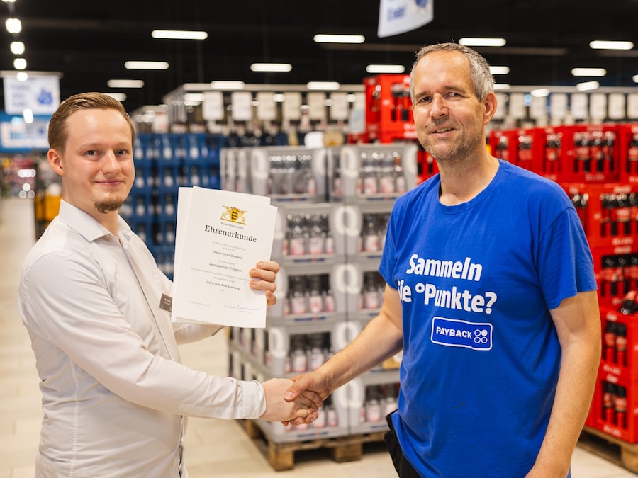 2 Männer stehen vor Getränkekisten und geben sich die Hand.