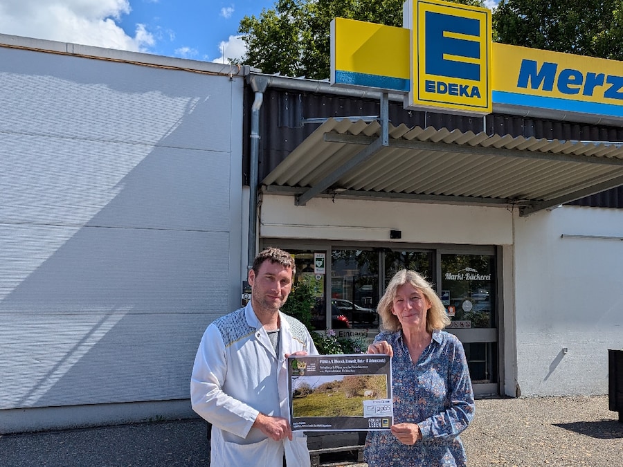 Ein Mann und eine Frau halten einen symbolischen Scheck und stehen vor einem EDEKA Markt.
