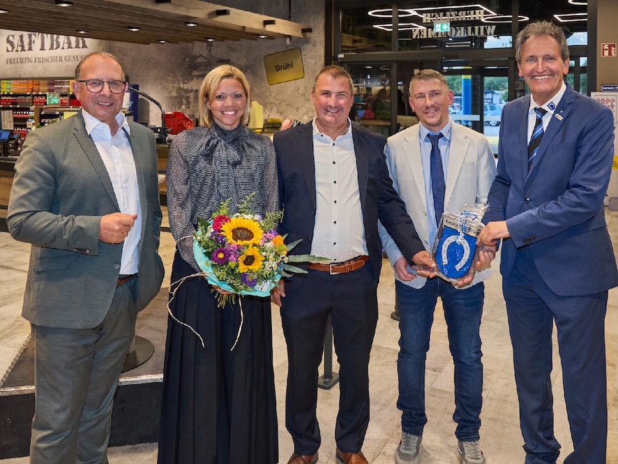 4 Männer und 1 Frau mit Blumenstrauß stehen im Foyer eines Marktes