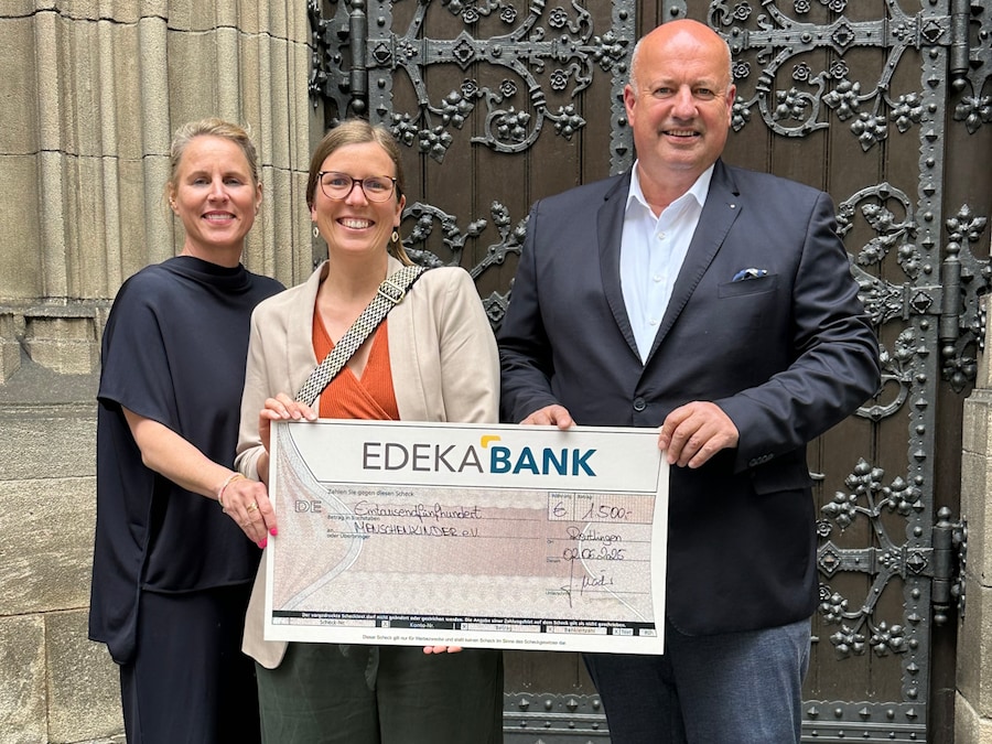 Drei Personen mit Scheck vor einem Tor