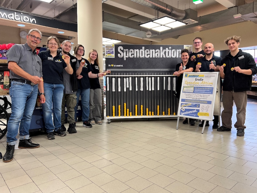 9 MItarbeitende des E centers stehen vor einer Spendenwand im Marktfoyer