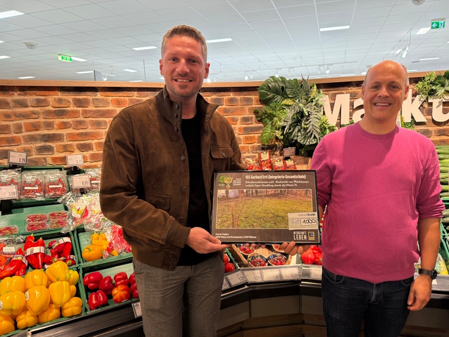 Zwei Männer stehen in der Gemüseabteilung und halten gemeinsam einen symbolischen Spendenscheck in Höhe von 1.000 Euro. 