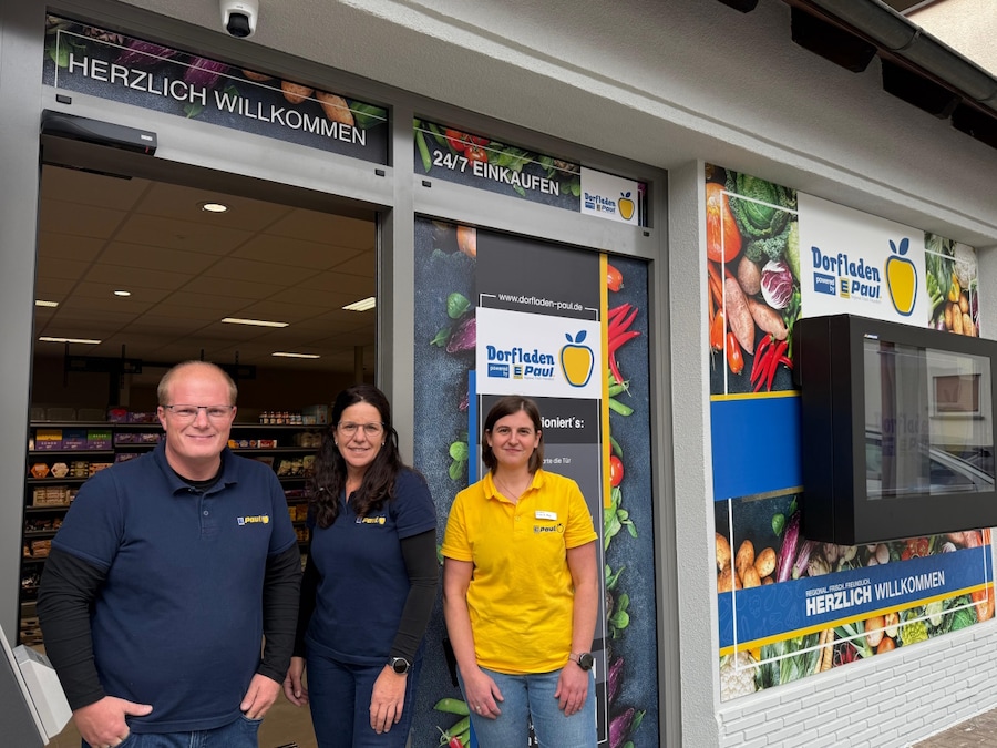 Ein Mann und 2 Frauen stehen vor dem Eingang des neuen Marktes