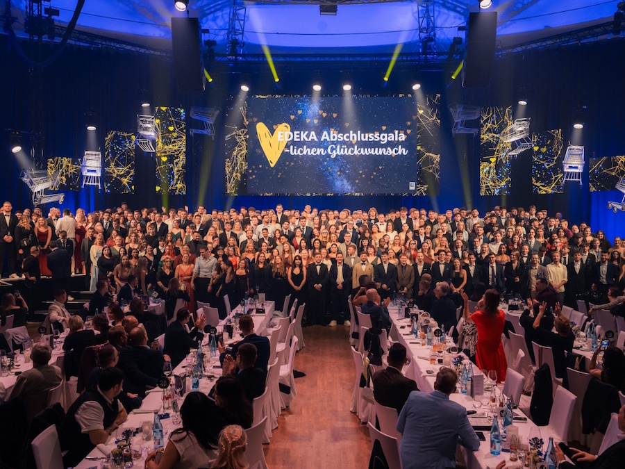 Ein großer Saal, über 300 festlich gekleideten Absolventen stehen auf der Bühne, davor Tischreihen mit Gästen.