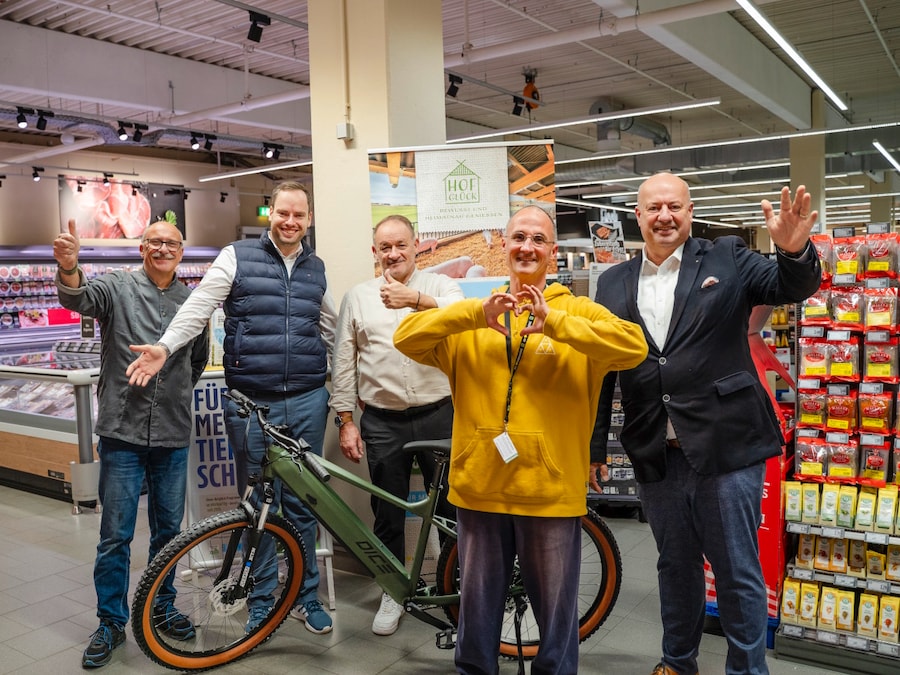 Fünf strahlende Männer stehen in einem großen EDEKA-Markt mit einem neuen E-Bike, das übergeben wurde. 
