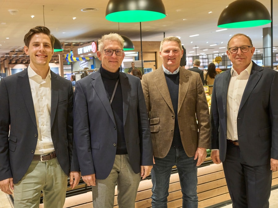Vier Männer in Jackets stehen nebeneinander in der Obstabteilung des modernisierten EDEKA-Markts und lächeln in die Kamera.
