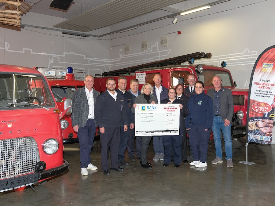 Eine Gruppe von 11 Personen steht mit einem symbolischen Spendenscheck in einer Feuerwehrhalle.