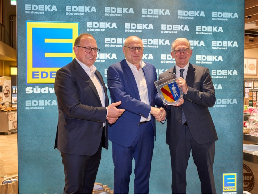 3 Männer stehen mit Stadtwappen in der Hand vor einer EDEKA-Wand im Markt.