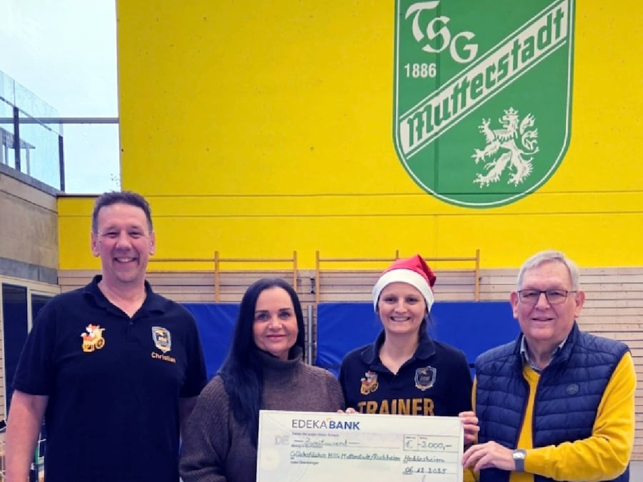 2 Männer und 2 Frauen stehen in einer Turnhalle mit einem symbolischen Scheck in den Händen.