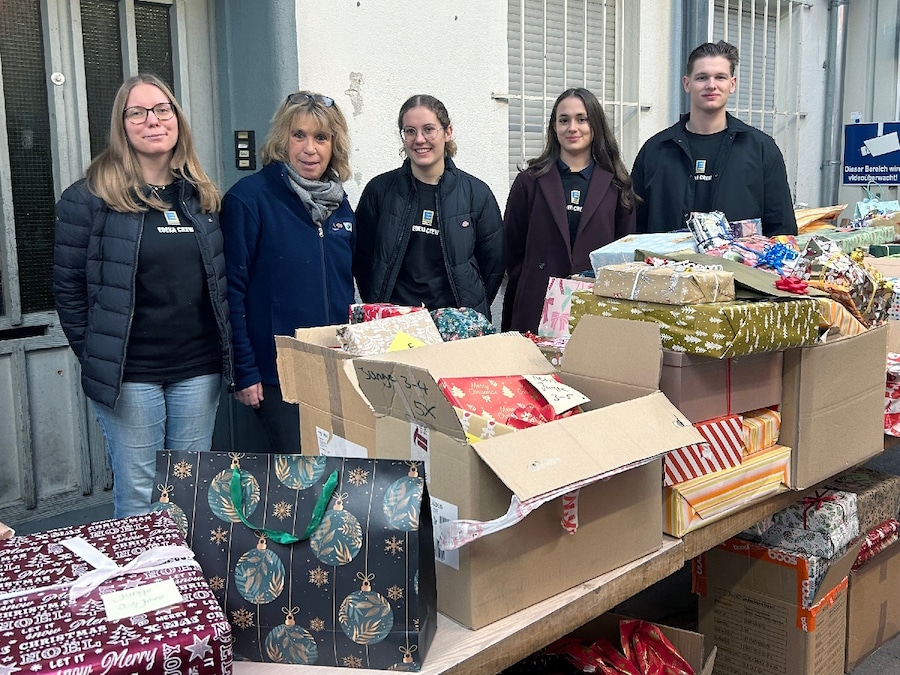 4 Frauen und 1 Mann stehen vor einem langen Tisch von Geschenken und Kartons.