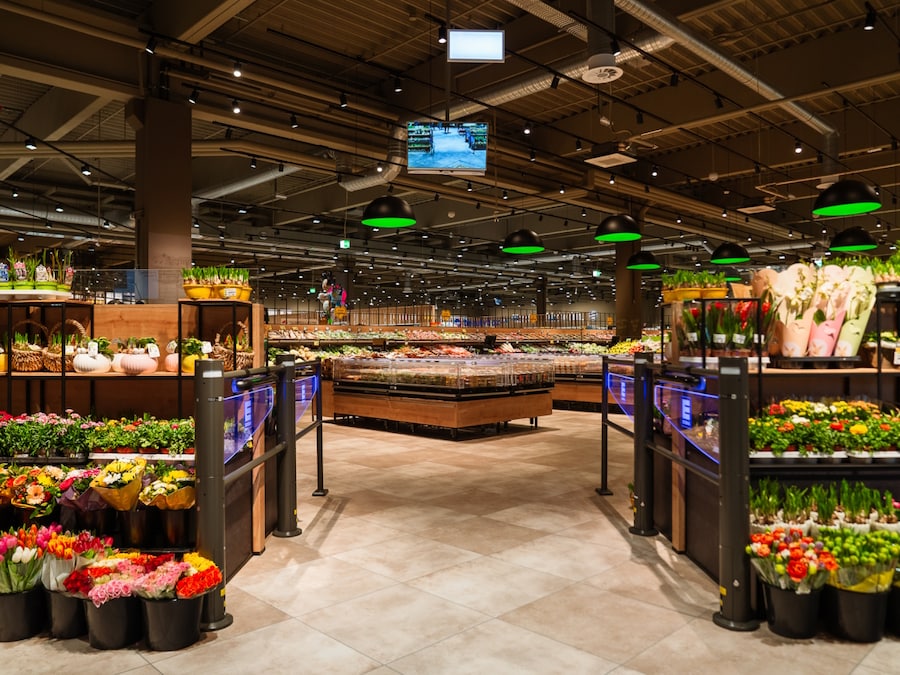 Eingang zur Obst- und Gemüseabteilung, links und rechts Blumen zum Verkauf, Blick auf einen großzügigen Markt