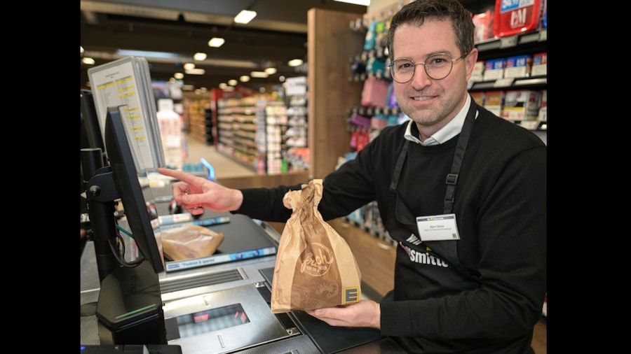 Ein Mann sitzt an der Kasse, hält eine Tüte in der Hand und bedient das Touch-Display.