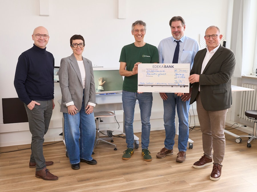 1 Frau und 4 Männer stehen mit einem symbolischen Scheck in einem Arztzimmer. 