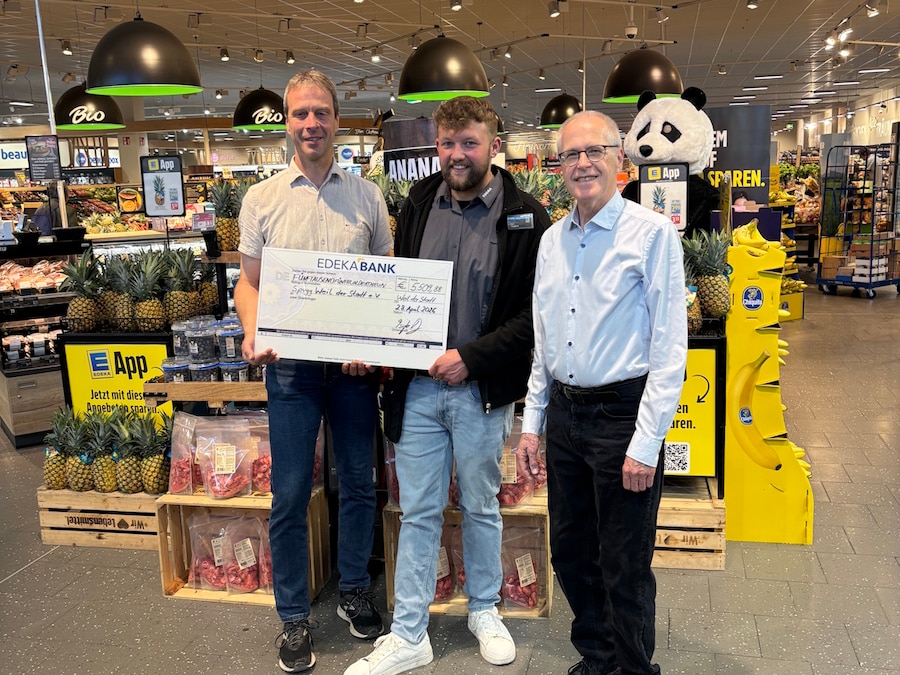 3 Männer stehen in der Obstabteilung eines EDEKA-Marktes, 2 davon halten einen symbolischen Spendenscheck