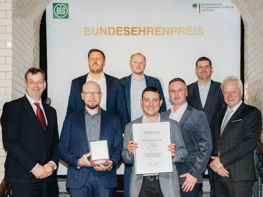 Acht Männer stehen mit dem Preis und der Ehrenurkunde auf einer Treppe.