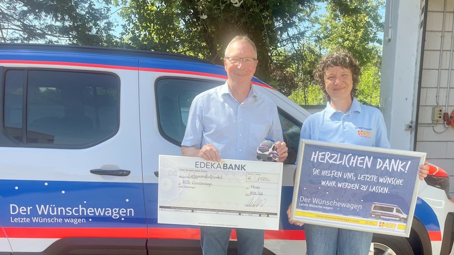 Ein Mann mit eine symbolischen Spendenscheck und eine Frau mit einem Plakat stehen vor dem Krankentransporter 