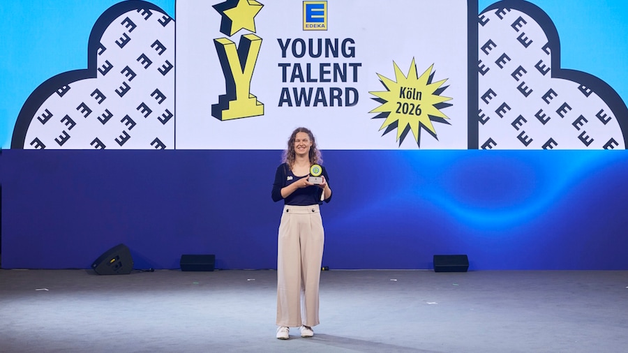 Eine lächelnde junge Frau steht auf der Bühne und hält stolz ihre Trophäe hoch. An der Wand steht Young Talent Award