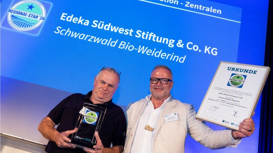 2 Männer halten einen Pokal und eine Urkunde vor einer großen Leinwand.