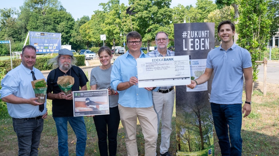 Eine Frau und 4 Männer stehen mit einem symbolischem Scheck und Kräutertöpfen auf einer Wiese.
