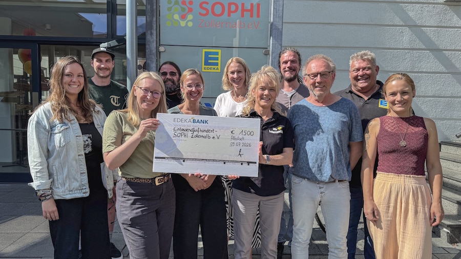 11 Personen stehen mit einem symbolischen Spendenscheck vor einem EDEKA Markt.