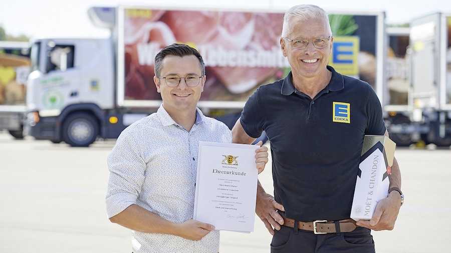Zwei Männer stehen mit einer Urkunde und Präsent vor einem LKW.