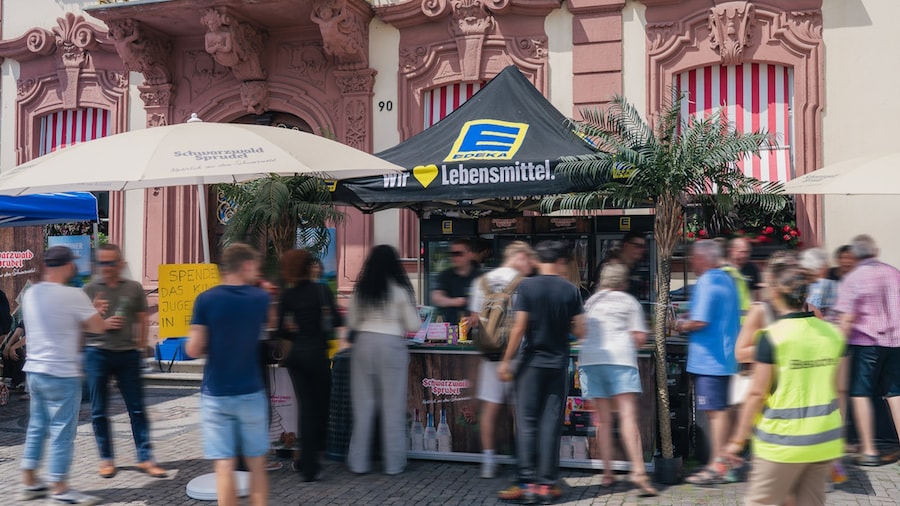 Viele Personen stehen an einem Stand mit EDEKA-Marktschirm