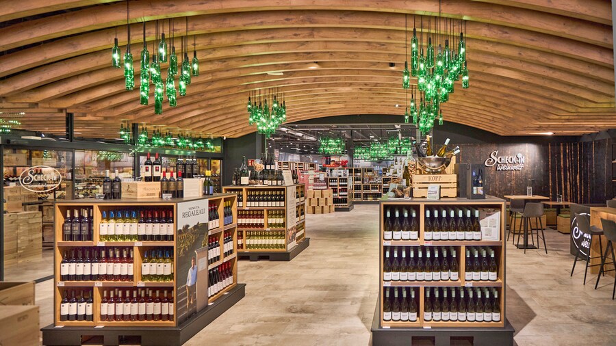 Weinabteilung im Vinothek-Stil mit Holzgewölbe und Hängeleuchten aus grünen Weinflaschen.